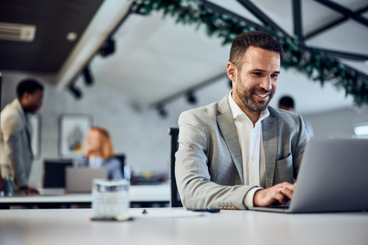 A smiling businessman working at the co-working space, typing an email to one of his clients.